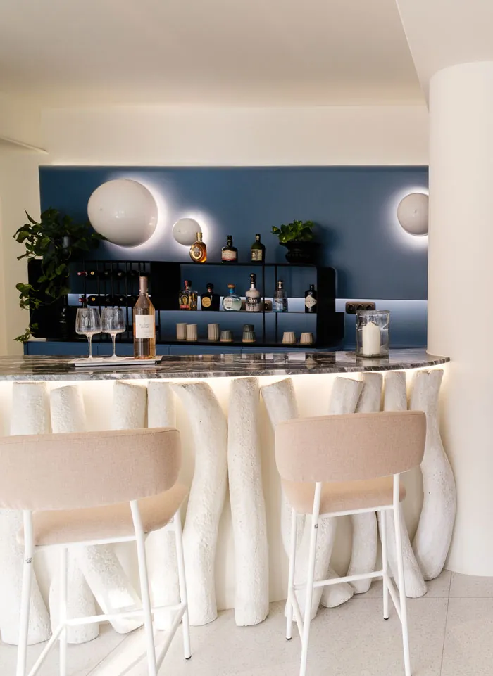 Το lobby bar: ανοιχτόχρωμος πάγκος και σκαμπό μπροστά σε βαθύ μπλε τοίχο με φιάλες